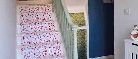 A staircase with white steps and red floral patterns, leading to a room with blue walls and a framed picture on the wall.