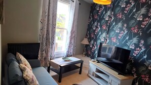 Una sala de estar con un sofá, un televisor sobre un mueble, una mesa con un tazón y cortinas con estampado floral.