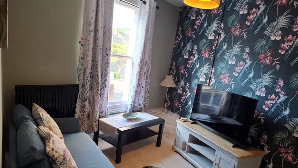 Een woonkamer met een bank, een televisie op een kast, een tafel met een schaal, en bloemen gordijnen.