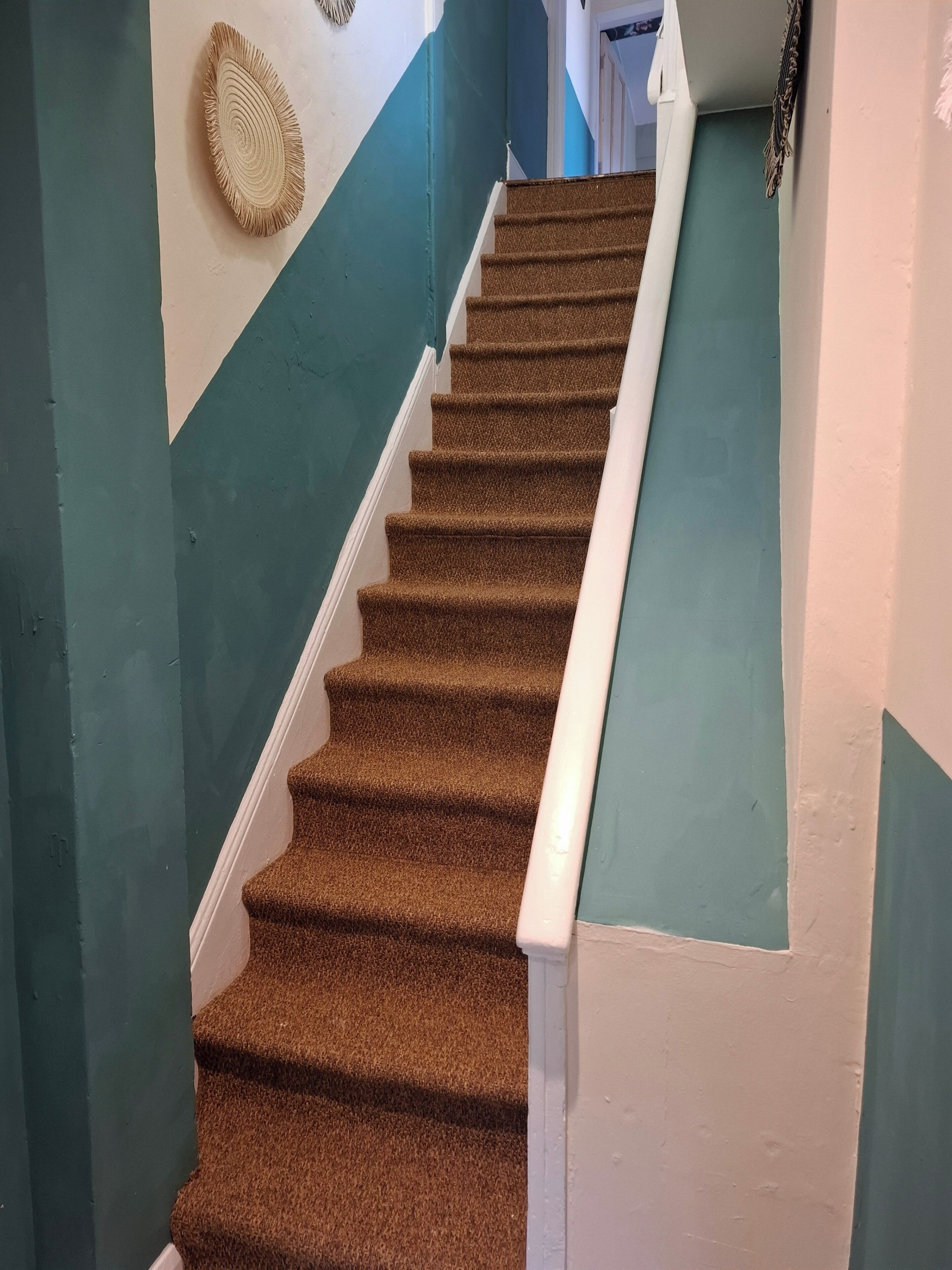 A carpeted staircase with white handrails, teal walls, and a decorative wall hanging.