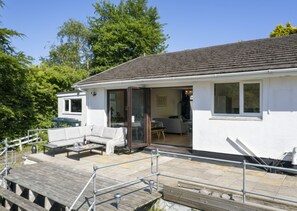 A white building with a tiled roof, a wooden deck, and a glass door leading to an interior with a sofa and a dining table. - A perfect for a relaxing getaway with family or friends (Tenby, Pembrokeshire)