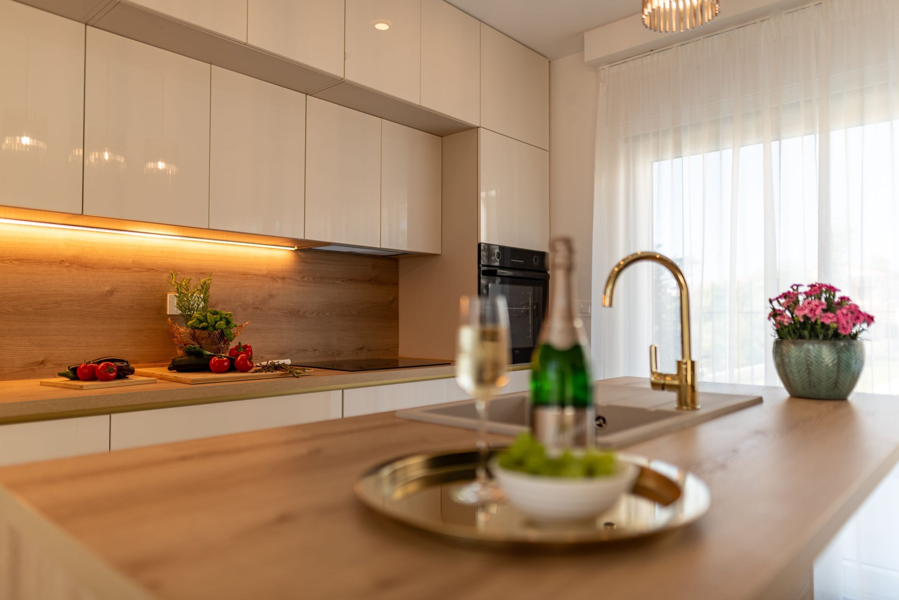 Eine moderne Küche mit weißen Schränken, einer Holz Arbeitsplatte, einem eingebauten Backofen und einem Spülbecken mit goldenem Wasserhahn.