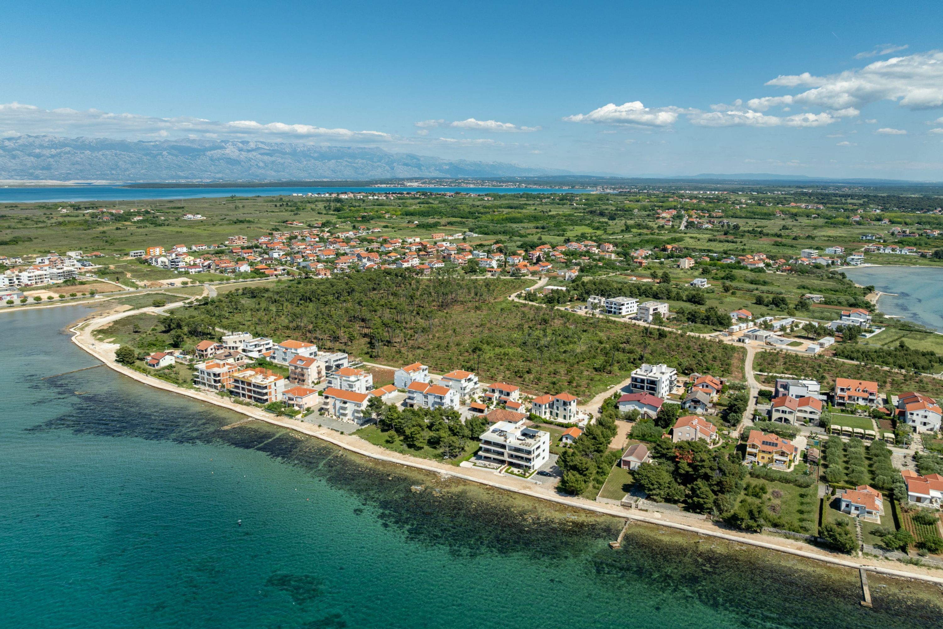 Luftaufnahme einer Küstenstadt mit Wohngebäuden, einem Strand und einer Bergkulisse.