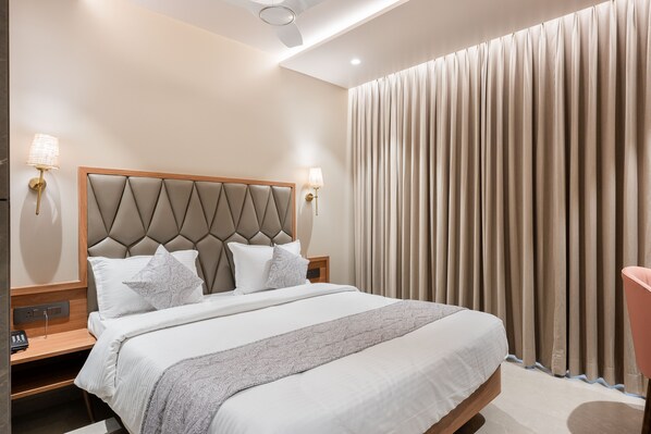 A hotel room with a large bed, two bedside lamps, a ceiling fan, and a view of the outside through curtains. - Nine Square Residency (Mumbai)
