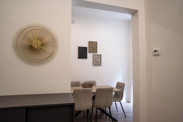 A modern dining area with a round table, cushioned chairs, and a wall-mounted decorative light fixture.