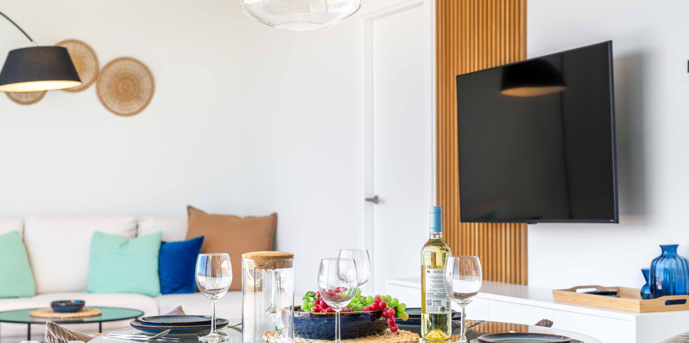 A modern dining area with a table set for two, a bottle of wine, and a television mounted on the wall.