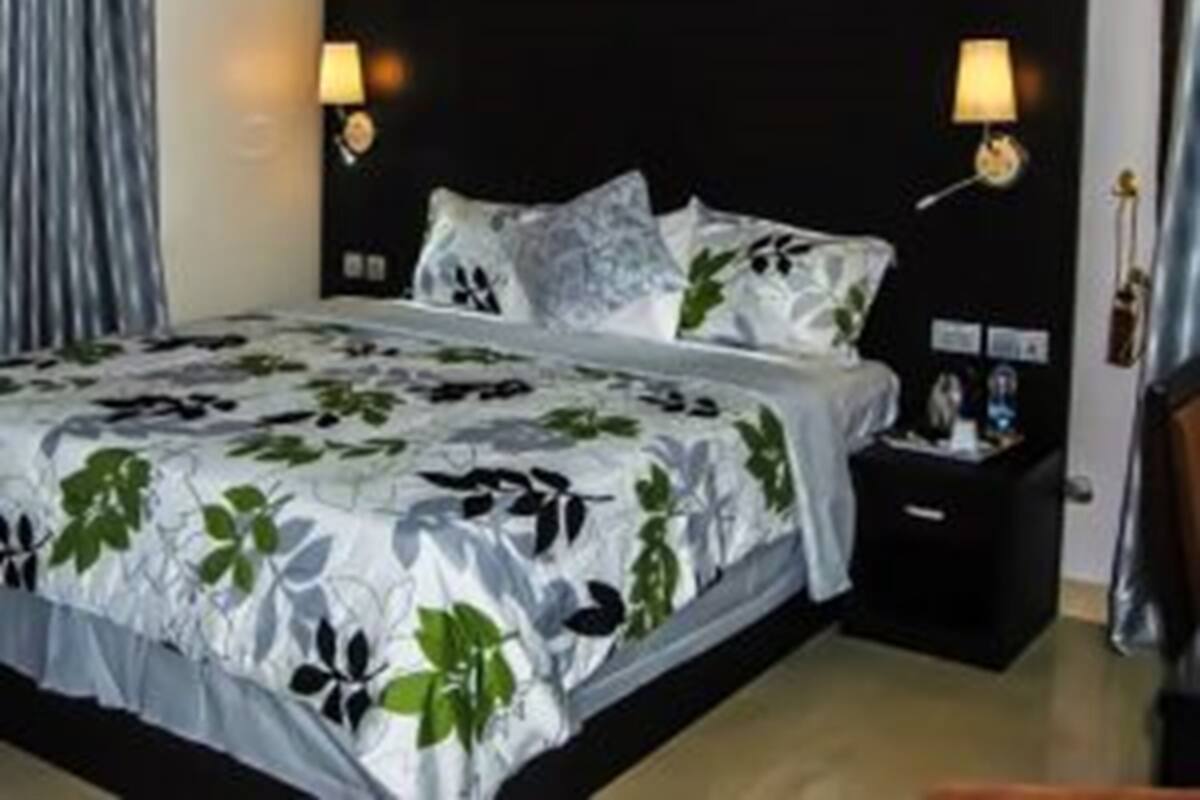 Una habitación de hotel con una cama grande, dos lámparas de noche, una mesita de noche y una ventana con cortinas.