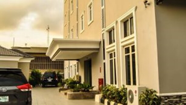 A multi-story building with a flat roof, a covered entrance, and a parking area with cars. - Royal Jatoz Hotel and Suites (Lagos)
