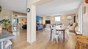 A spacious living area with a dining table, chairs, and a sofa. There is a TV mounted on the wall and a clock on the wall. - Large family villa with shaded terraces, garden and swimming pool (Lédenon)