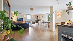 A spacious living area with a wooden floor, a sofa, a dining table with chairs, and a kitchen area with a dishwasher. - Large family villa with shaded terraces, garden and swimming pool (Lédenon)