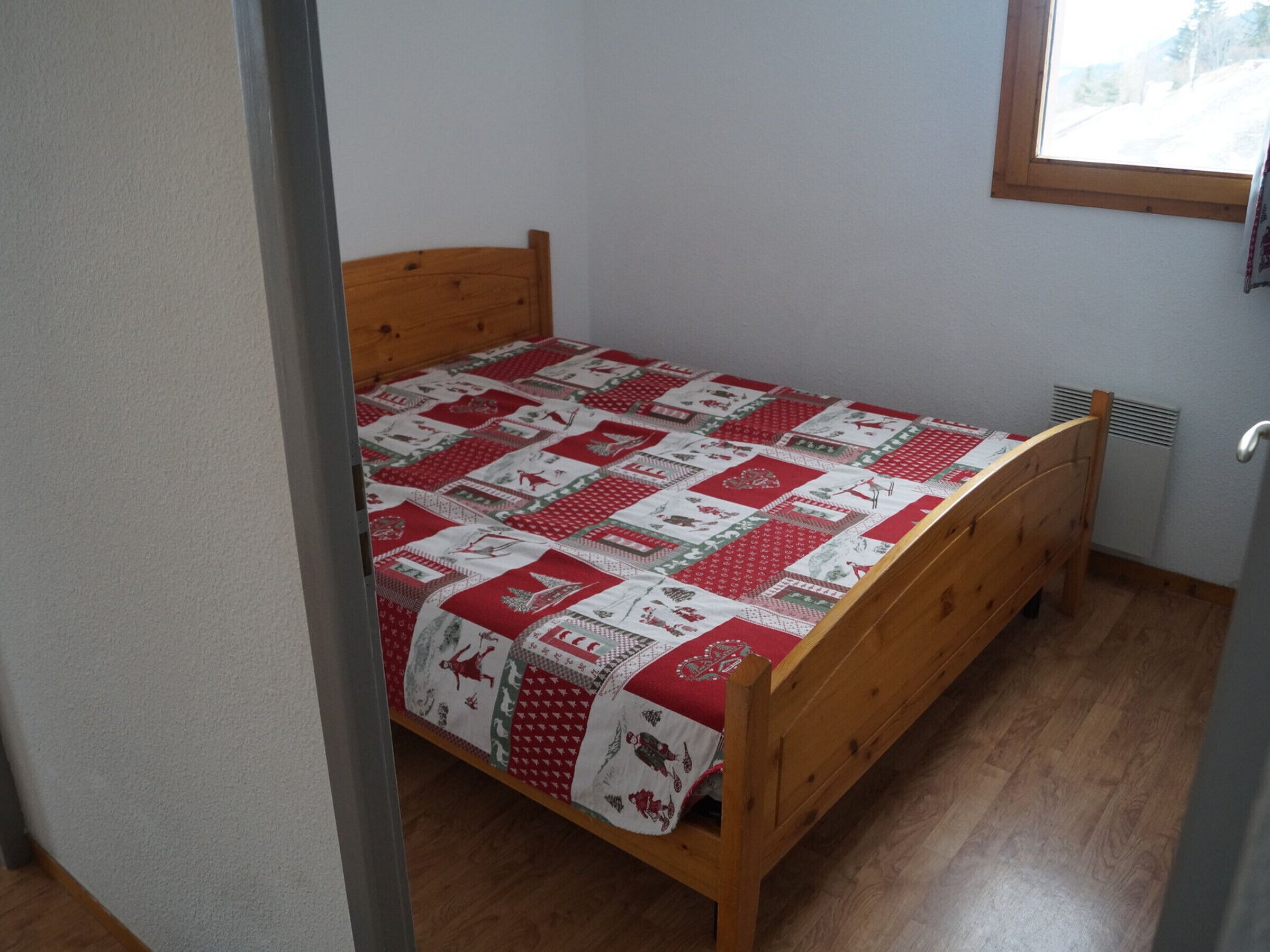 Una habitación pequeña con una cama individual, estructura de madera y colcha roja y blanca.