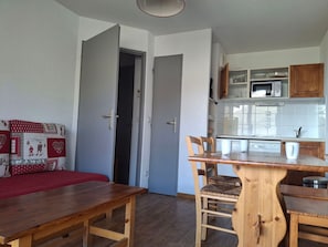 Kompakti oleskelutila, jossa on ruokailualue, valkoisilla kaapeilla varustettu keittiö ja ovi, joka johtaa toiseen huoneeseen.