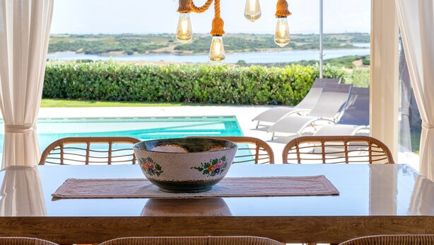 A dining table with a bowl, chairs, and a view of a pool and landscape. - Holiday Home 'Flora Sea View' with Sea View, Wi-Fi and Air Conditioning (Punta de su Torrione)