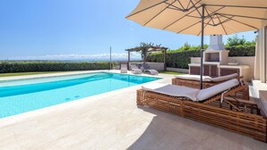 A swimming pool with lounge chairs and an umbrella, a pergola with plants, and a view of the sea. - Holiday Home 'Flora Sea View' with Sea View, Wi-Fi and Air Conditioning (Punta de su Torrione)