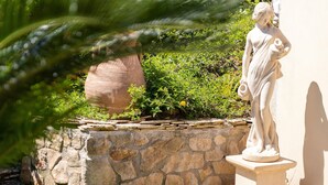 A statue in a garden setting with a stone wall and greenery. - Holiday Home 'Flora Sea View' with Sea View, Wi-Fi and Air Conditioning (Punta de su Torrione)