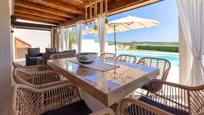 A wooden ceiling, wicker chairs, a glass table, and a view of a swimming pool. - Holiday Home 'Flora Sea View' with Sea View, Wi-Fi and Air Conditioning (Punta de su Torrione)