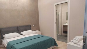 A bedroom with a bed, a nightstand, a bathroom visible through an open door, and a stack of towels on a cabinet. - BUNKER DEGLI INVENTORI SRLS (Foggia)