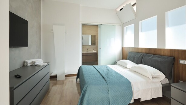 A modern bedroom with a bed, bedside tables, a TV, and a bathroom visible through an open door. - BUNKER DEGLI INVENTORI SRLS (Foggia)