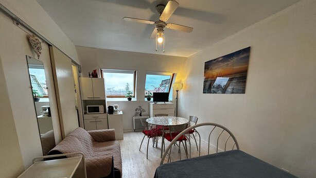 Une pièce de taille modeste comprenant un lit, un petit coin cuisine, une table à manger avec des chaises et un ventilateur de plafond.