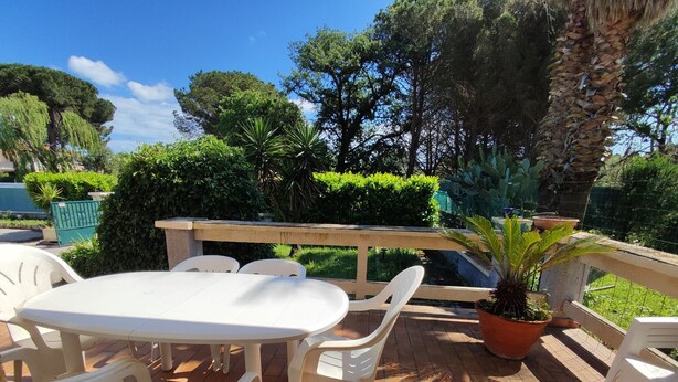 An outdoor patio with a round table and white plastic chairs, surrounded by potted plants and a wooden railing. - Air-conditioned villa with large garden, pets allowed (Palau-del-Vidre)