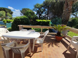 Un patio al aire libre con una mesa redonda y sillas de plástico blanco, rodeado de plantas en macetas y una barandilla de madera.