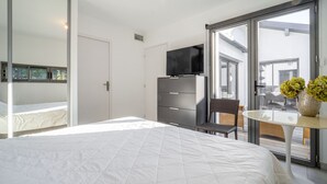 Ein Schlafzimmer mit einem großen Bett, einem Fernseher auf einer Kommode, einem Sessel und einem Tisch mit Blumen.