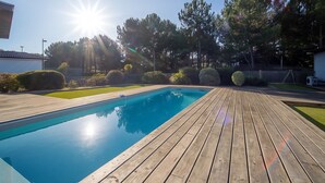 Eine Holzterrasse umgibt einen rechteckigen Pool mit glasklar blauem Wasser.