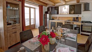 Una cocina compacta con electrodomésticos modernos, un comedor con una mesa dispuesta para dos personas, y vistas al exterior a través de un ventanal.