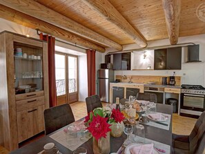 A compact kitchen with modern appliances, a dining area with a table set for two, and a view of the outside through a glass door.