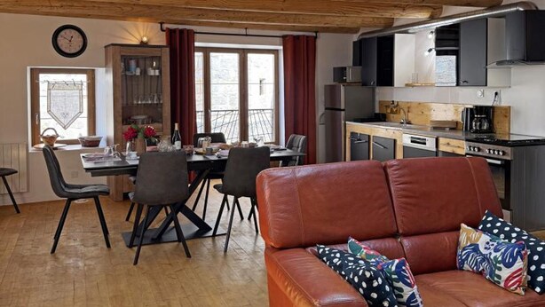 Una sala acogedora con un sofá de cuero, una mesa de comedor con sillas, una cocina con electrodomésticos modernos y un ventanal grande.