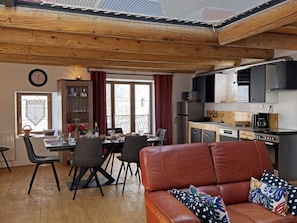 A cozy living area with a leather sofa, a dining table with chairs, a kitchen with modern appliances, and a large window.