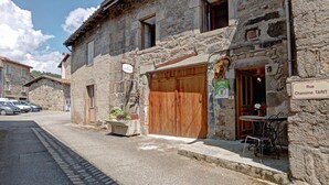 Un edificio de piedra con puerta de madera, un cartel que indica 'Rue Chanoine TARIT' y un pequeño espacio al aire libre con mesas y sillas.