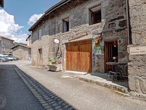 A stone building with a wooden door, a sign indicating 'Rue Chanoine TARIT,' and a small outdoor seating area with tables and chairs.