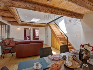 A cozy room with a wooden ceiling, a sofa, a dining table with a meal, and a staircase.