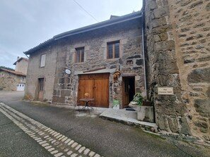 A stone building with a wooden door and a small outdoor seating area.