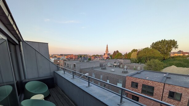 Een terras op het dak met uitzicht op een kerktoren en omliggende gebouwen.