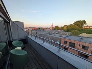Een terras op het dak met uitzicht op een kerktoren en omliggende gebouwen.