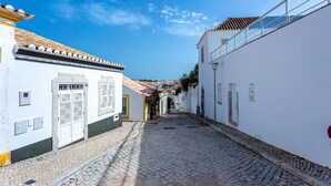 A cobblestone street flanked by white buildings with traditional architecture, including a tiled roof and a balcony.