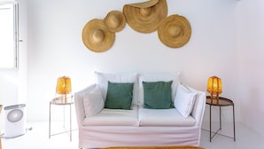 A white sofa with green and white cushions, two small tables with lamps, and a wall with woven wall art.