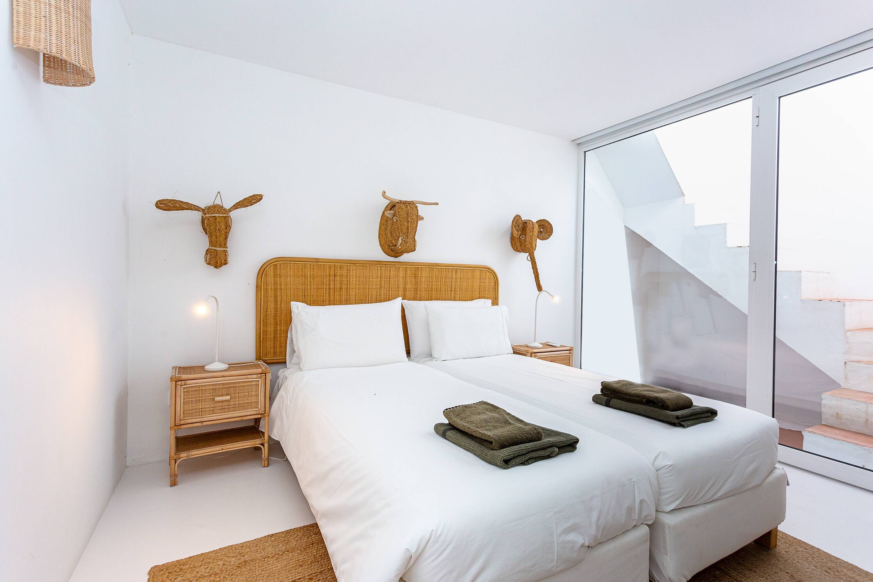 A modern bedroom with a large bed, two nightstands, a woven headboard, and decorative wall art.