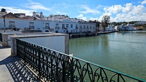 A riverside walkway with white buildings, a metal railing, and a boat docked on the water.
