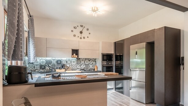 Een moderne keuken met een centraal eiland, roestvrijstalen apparatuur en een decoratieve klok aan de muur.