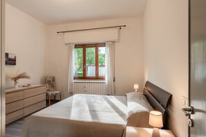 A bedroom with a bed, bedside lamps, a window with curtains, a dresser, and a chair.