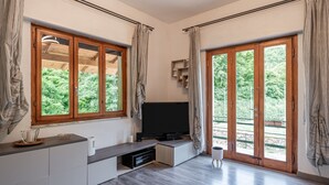 Een moderne woonkamer met een flatscreen televisie, inbouwplanken en grote ramen met gordijnen.