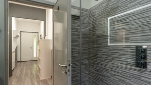 Een modern interieur met een houten vloer, een glazen deur die leidt naar een gang, en een gestructureerde wand met een ingebouwd bedieningspaneel.