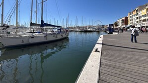 Un puerto deportivo con veleros amarrados, un muelle de madera y edificios al fondo.