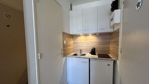 Cocina compacta con armarios blancos, un lavamanos, cafetera y microondas integrado.