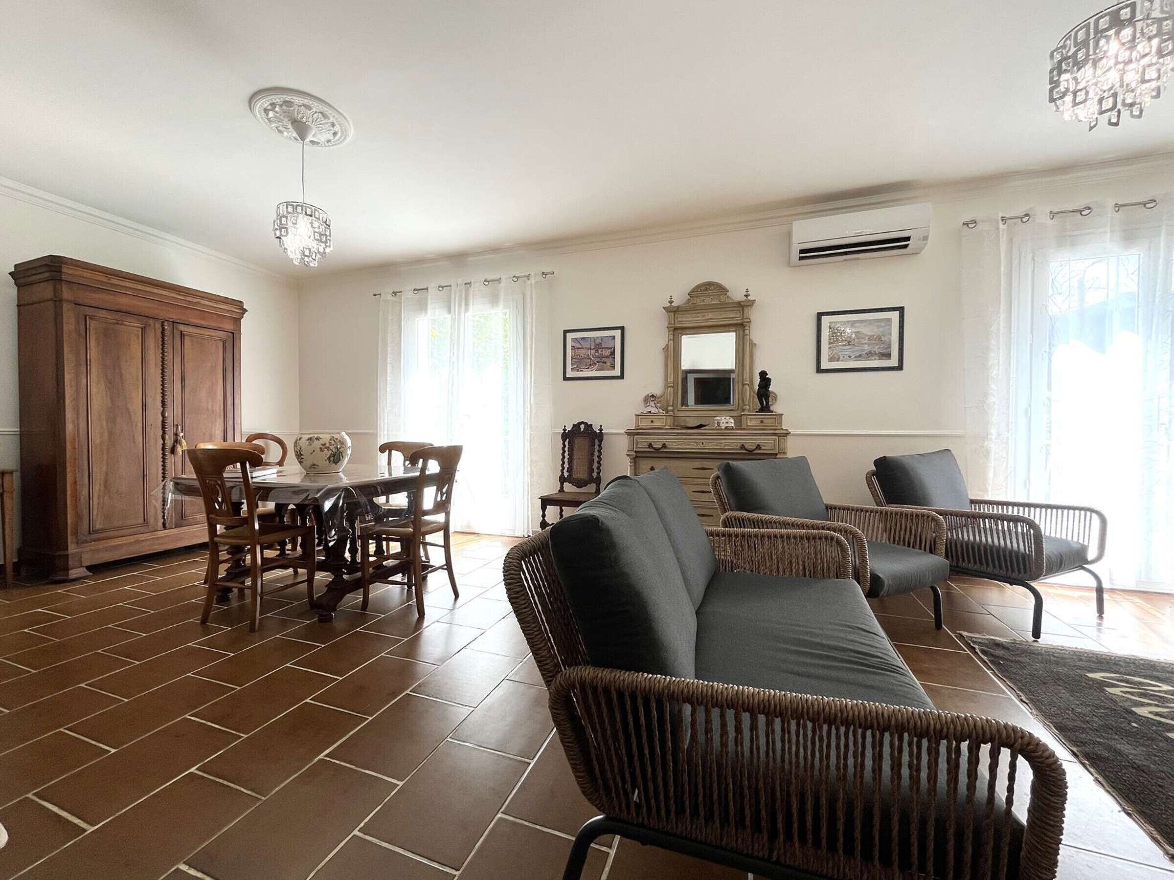 A spacious living room with a dining area, wicker furniture, a large cabinet, and a chandelier.