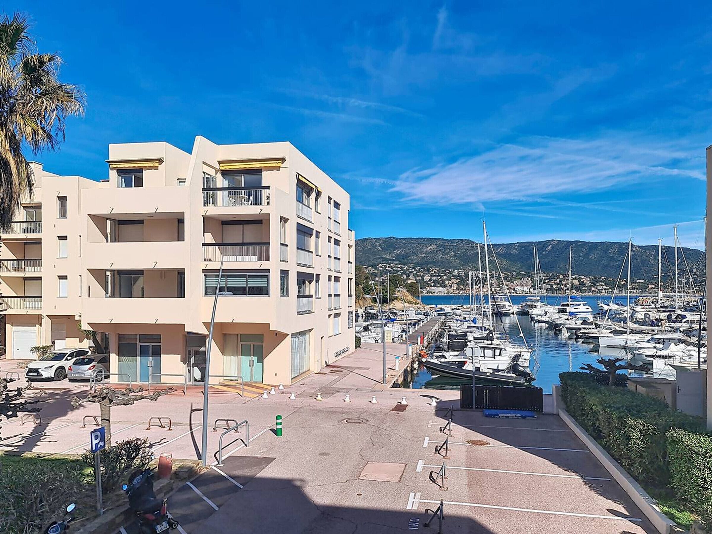 A marina with boats, a parking area, and a multi-story building with balconies.