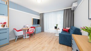 Una sala moderna con un sofá azul, un comedor con sillas rojas y blancas, un televisor y una pequeña mesa con una computadora portátil.